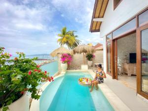 a woman sitting on the edge of a swimming pool at Bali Secrets Oceanfront Villas in Candidasa