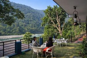 two women sitting at tables with a view of a river at Riverline Gold Resort in Rishīkesh