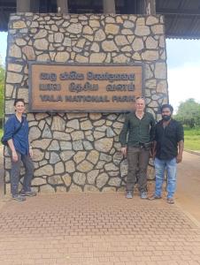 three people standing in front of a stone wall at lake paradise cabana in Tissamaharama