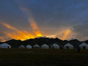 a group of white tents in a field with a sunset at Kel-Suu Kyrgyzstan Yurt Camp in Kol-Suu