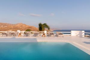 a swimming pool with chairs and a table and the ocean at Princess Villas Oasis Mykonos in Kalafatis
