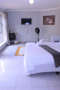 a white bedroom with two beds and a television at Fargon Guest House in Polokwane