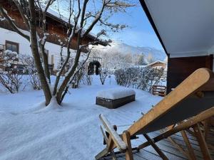 a snow covered yard with a bench and a tree at Achentaler Auszeit in Schleching