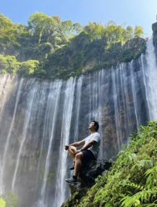 a man sitting on a rock in front of a waterfall at Neomi Homestay Malang in Wendit