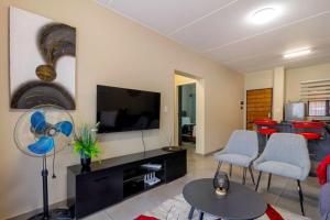 a living room with a tv and a couch and chairs at The Waterfallcity Charm next to Mall of Africa in Midrand