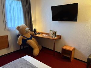 a teddy bear sitting at a desk in a hotel room at Brit Hotel Confort Villeneuve Sur Lot in Bias +20 photos
