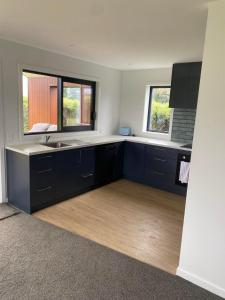 an empty kitchen with blue cabinets and two windows at Pukutahi Palms in Te Anau +5 photos