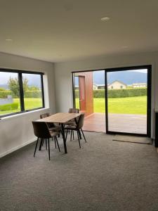 a dining room with a table and chairs and windows at Pukutahi Palms in Te Anau
