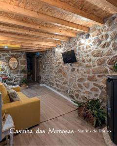 a living room with a stone wall with a couch and a tv at Casinha das Mimosas in Sanfins do Douro