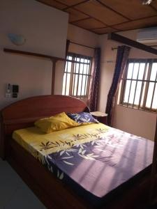 ein Schlafzimmer mit einem Bett mit Holzrahmen und Fenstern in der Unterkunft Godfils in Abomey-Calavi