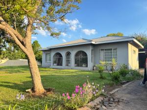 a house with a tree and flowers in the yard at SashMc Flair Guesthouse in Klerksdorp