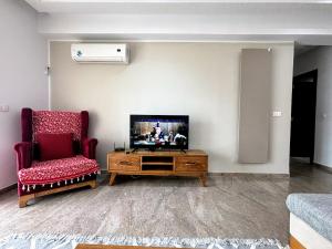 a living room with a flat screen tv and a chair at Abilia Apt - À Proximité de l'Aéroport - Parking gratuit et Wi-Fi rapide in Sukrah