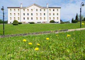 a large white building with a field of yellow flowers at Phi Hotel Astoria in Susegana
