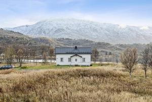 a white house in a field with a mountain in the background at The house in Vika in Lødingen
