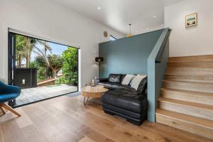 a living room with a black leather couch and stairs at Up Above The Crescent in Waihi Beach