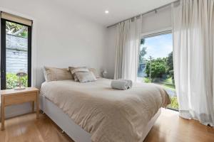 a white bedroom with a bed and a large window at Up Above The Crescent in Waihi Beach +14 photos