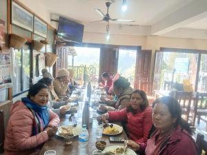 a group of people sitting at a long table in a restaurant at Hotel small town guest house in Bandipur