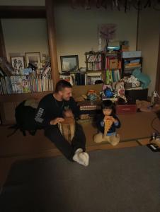 a man sitting in a living room with two dolls at Satoyama Guest House Couture in Ayabe