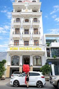 a woman standing in front of a building with a car and balloons at Kim Hoàn Hotel Phan Rang in Phan Rang–Tháp Chàm