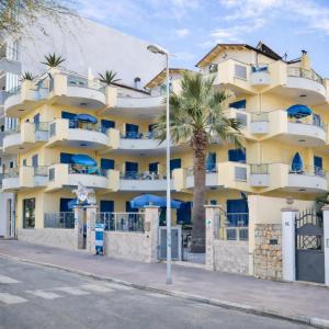 a yellow building with blue balconies and a palm tree at La Baia Di Ulisse in Venetico