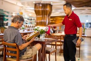 Ein Mann sitzt mit einem Kellner an einem Tisch in einem Restaurant in der Unterkunft Hotel Essencia in Dumaguete