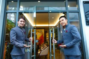 Dois homens de fato à frente de uma porta de vidro. em The Scarlett Boutique Hotel em Hue