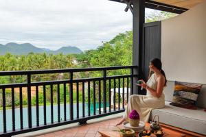 a woman sitting on a couch on a balcony looking at her cell phone at La Résidence Phou Vao in Luang Prabang