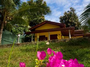 une petite maison jaune avec des fleurs roses au premier plan dans l'établissement Resort Like No Other, à Uggalboda