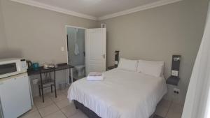 a bedroom with a white bed and a kitchen at Chrisserus Guest Rooms in Bloemfontein