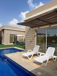 two chairs and a swimming pool next to a house at Blue Revan chalet in Salalah