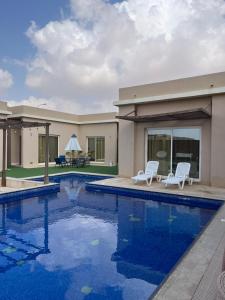 a swimming pool with two chairs and a house at Blue Revan chalet in Salalah