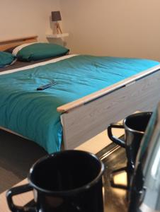 a bed with a blue blanket and two cups on a table at Hôtel de l'abbaye in Saint-Savin
