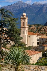 a building with a clock tower with mountains in the background at Résidence A Stella in Piana