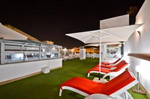 eine Terrasse mit roten und weißen Stühlen und einem Sonnenschirm in der Unterkunft The Zentral Arenal Suites in Sevilla
