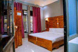 a bedroom with a bed with a wooden headboard and windows at EAR KEN BARHAM GUESTHOUSE in Rwumba