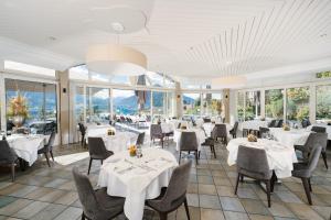 a restaurant with white tables and chairs and windows at Solbadhotel Sigriswil in Sigriswil