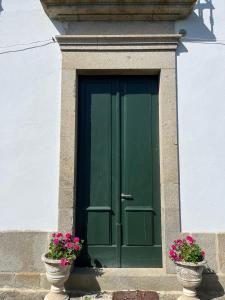 a green door in a white building with two pots of flowers at Casa da Freiria in Ponte de Lima