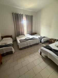 a hotel room with three beds and a window at Pousada Matriz 2 in Ouro Fino