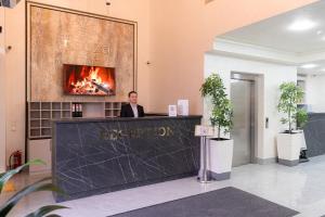 a man standing at a reception desk with a fireplace at Rauza Hotel Tashkent in Tashkent