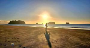 a person walking on the beach at sunset at Kupe Boutique House with ensuite free wifi in Whitianga