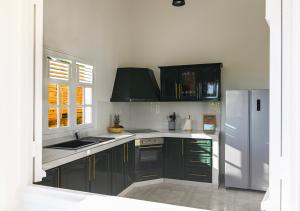 a kitchen with black cabinets and a stainless steel refrigerator at Villa Caryota, Panorama Montagnes & Piscine 9m in Le Marin