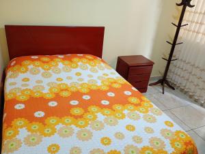 a bed with an orange comforter with flowers on it at Apartamentos en Huanchaco in Huanchaco
