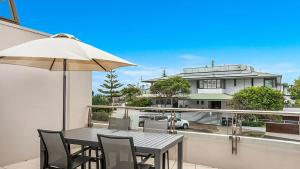 a patio table with chairs and an umbrella on a balcony at Pipi's On The Beach 1 - 2 Fletcher Street in Byron Bay