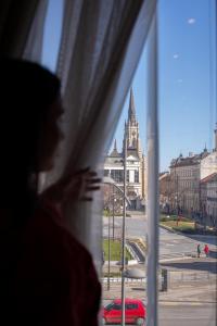 a woman looking out of a window at a church at Garni Hotel Centar in Novi Sad +47 photos