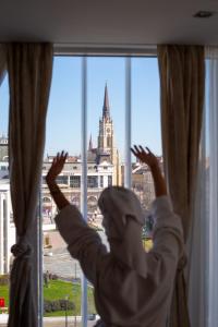 a person is looking out of a window at a building at Garni Hotel Centar in Novi Sad