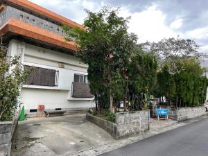 a white building with a tree next to a street at Kami House in Amami