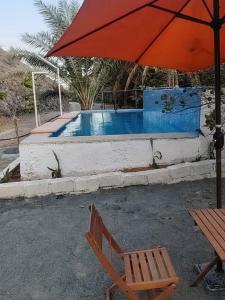 a red umbrella and a chair next to a pool at Hidden Valley GLAMPING in Fujairah
