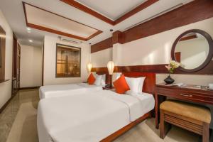 two beds in a room with a desk and a mirror at NA Hoian Hotel in Hoi An