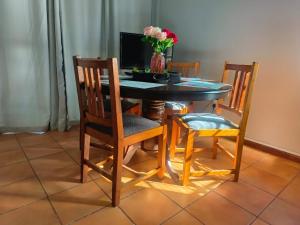 a dining room table with four chairs and a vase with flowers at LaBoezma Accommodation in Oudtshoorn