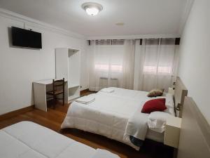 a bedroom with two beds and a desk and a television at Apartamentos Shalom Ribadeo in Ribadeo